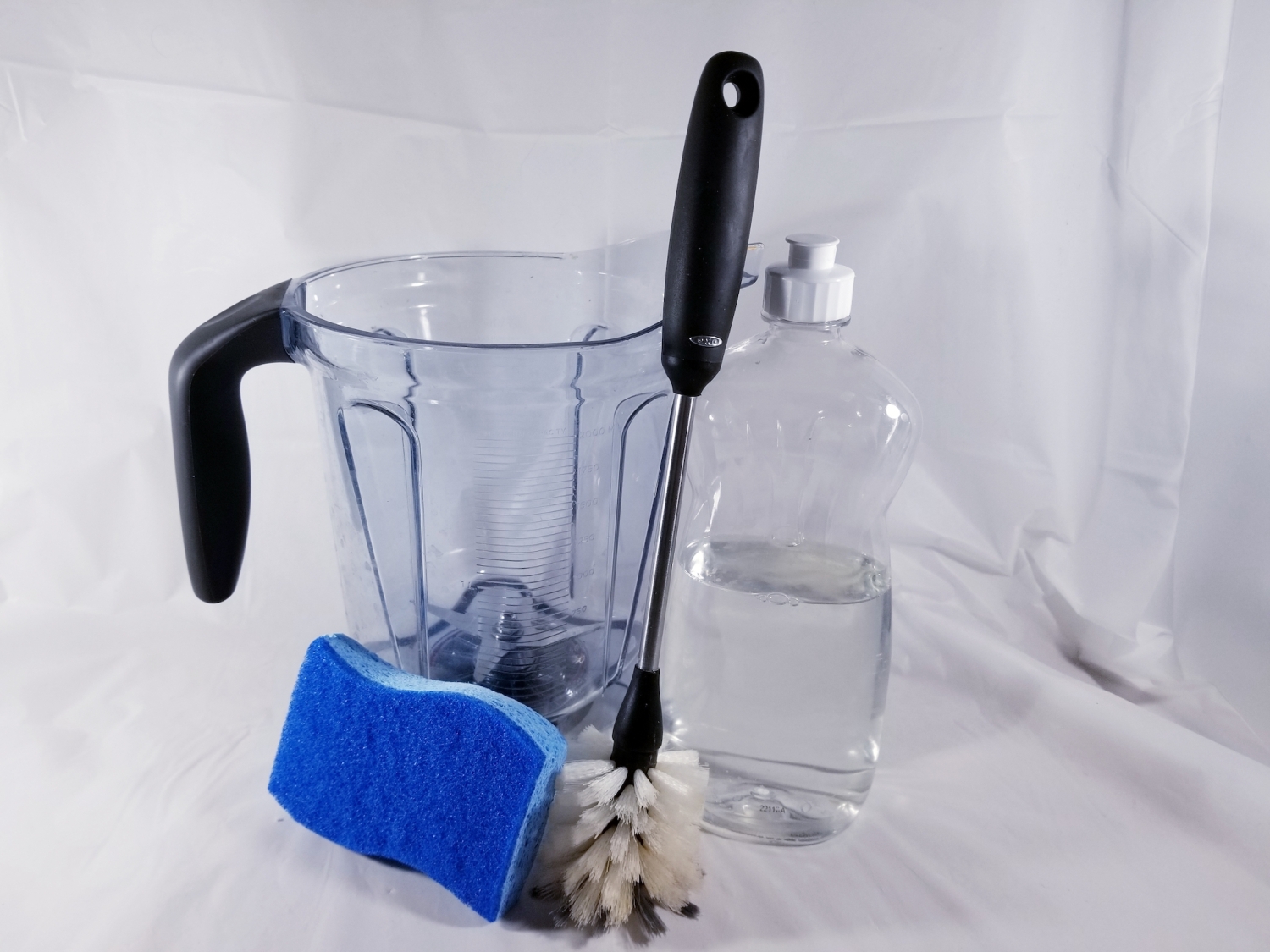 The blender container, a bottle of soap, a sponge, and a scrub brush