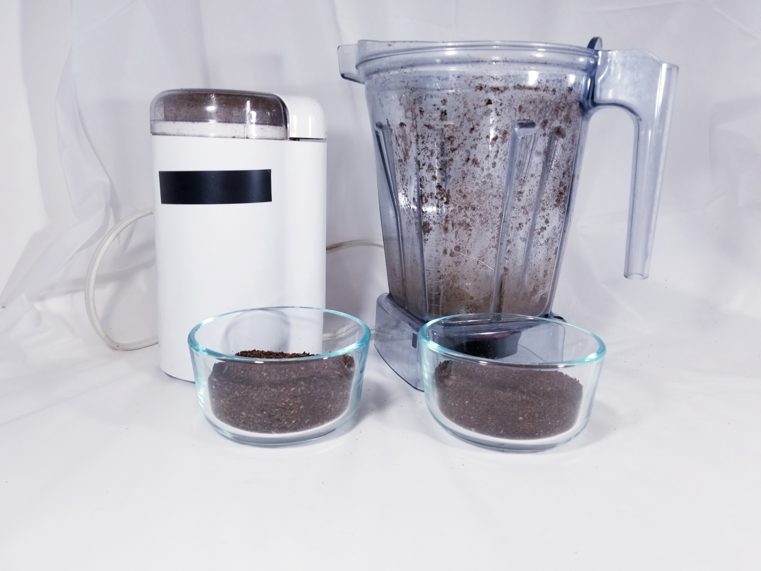 Photo of a coffee grinder, a blender container, and two containers of ground coffee